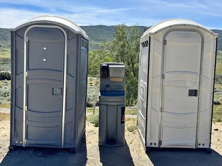 Two portable restrooms and a handwashing station on a graded work site