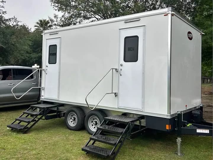 Two-stall restroom trailer set up on grass with its entry steps down