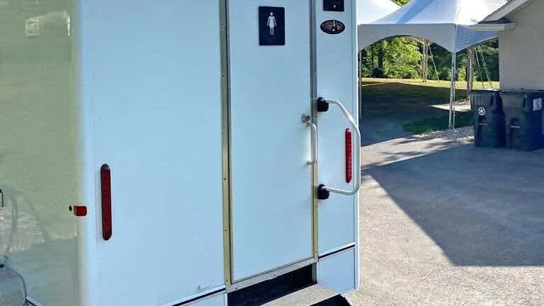 Restroom trailer parked beside a white event tent