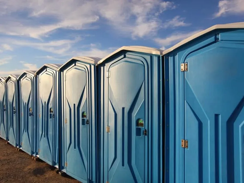 A long row of blue portable restrooms lined up under an open sky