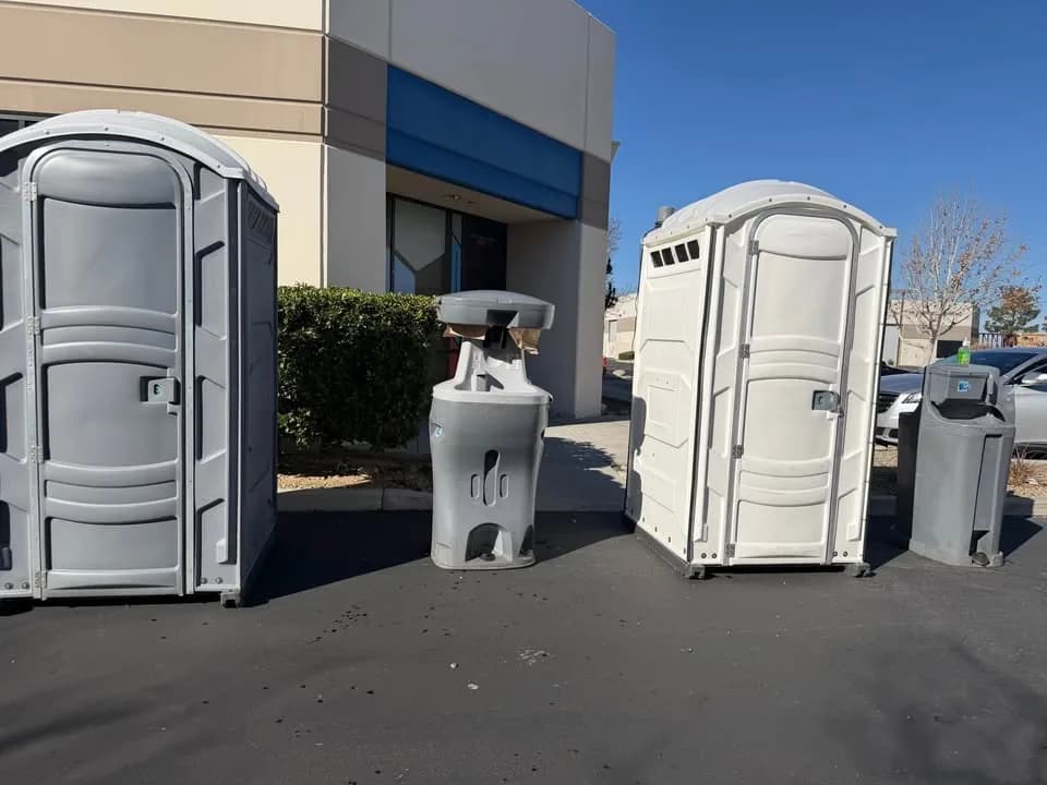 Freestanding handwashing station beside two portable restrooms